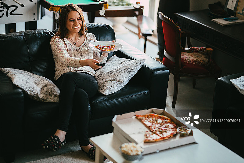 女人一边吃外卖披萨一边在家看电视图片素材