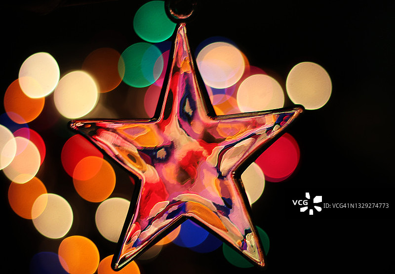 一个星星形状的圣诞装饰品的特写挂在散焦的彩色灯光上的黑色背景图片素材
