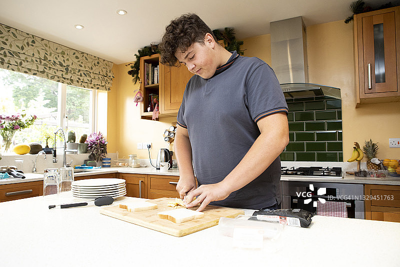 一个十几岁的男孩站在厨房里做火腿奶酪三明治图片素材