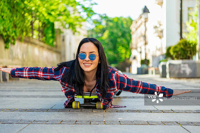 美丽的年轻女子滑冰骑在她的长板在城市。图片素材