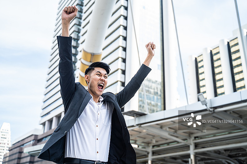 亚洲男人在城市里以幸福举手为得到新工作感到高兴。年轻的商人得知工作申请的面试测试结果是通过办公室工作后，感到高兴和自由图片素材