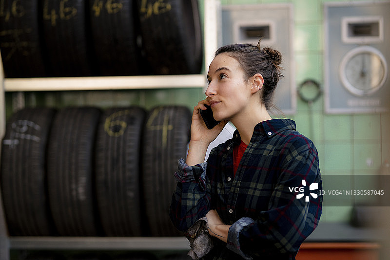 女机械师在车间的轮胎架旁讲手机时，目光移开图片素材