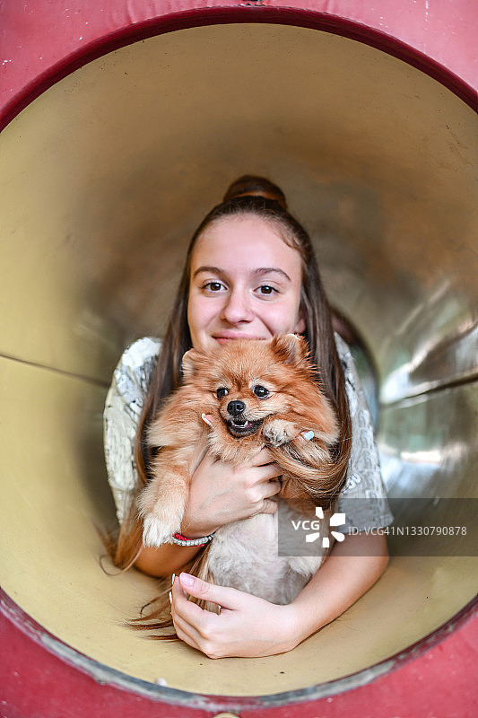 微笑的少女和狗爬过操场隧道图片素材
