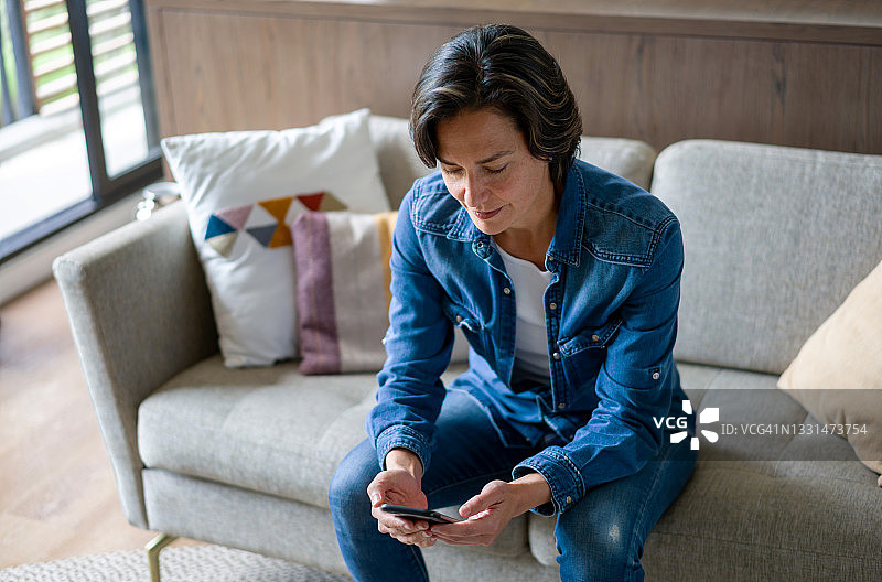 一个女人坐在沙发上用手机发短信图片素材