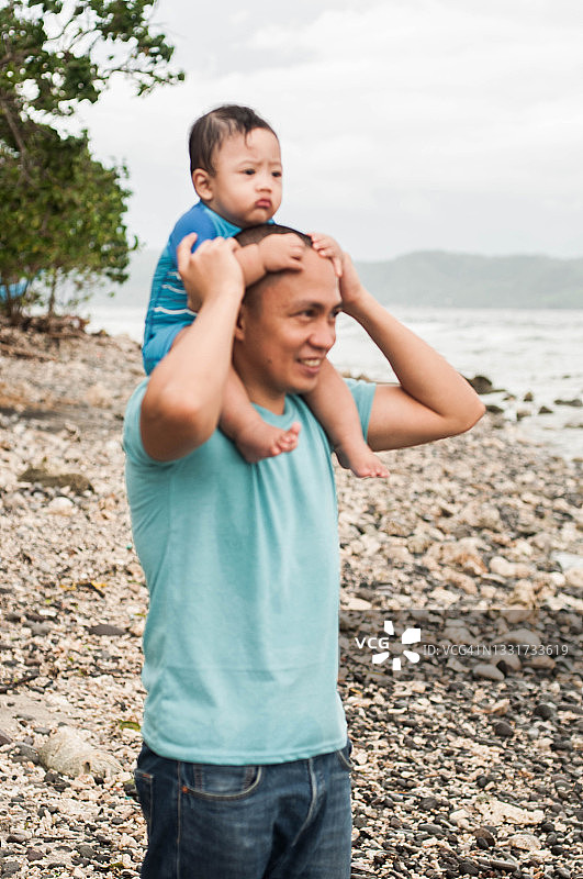 在沙滩上，一位年轻的东南亚父亲把儿子扛在肩上图片素材