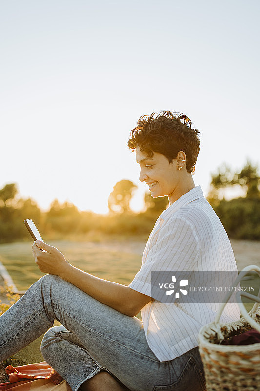 一个微笑的女人在日落野餐时使用智能手机图片素材