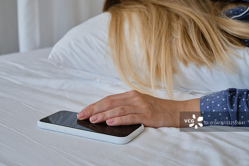 女孩在舒适的床上拿着智能手机，睡觉前或起床后查看社交网络账户。小玩意上瘾。女人用手机发短信图片素材