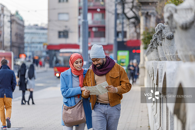 年轻的非洲男子和他的穆斯林妻子带着旅游地图在市区散步。图片素材