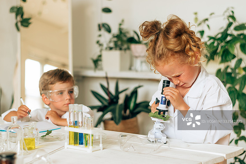穿着白色制服、戴着防护眼镜的男孩和女孩在家庭实验室里做化学实验。回到学校的概念。年轻的科学家。自然科学。儿童的学前和学校教育图片素材