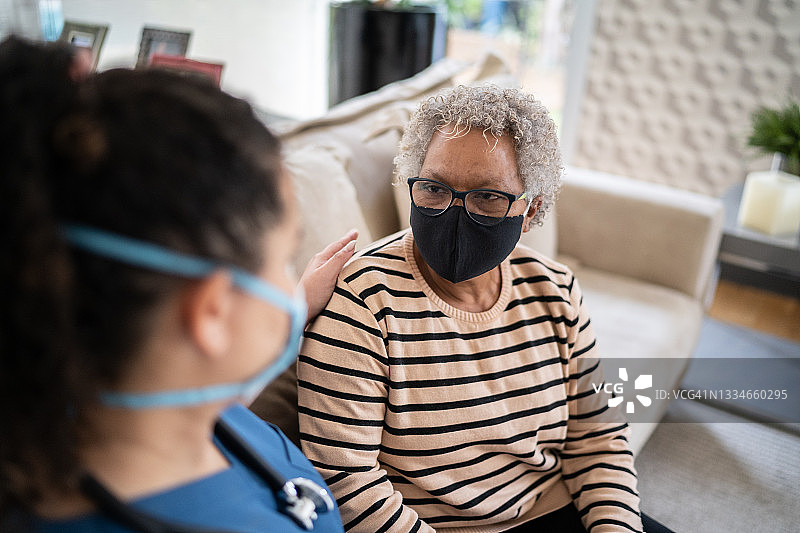 家庭护理员戴着防护口罩在家中与老年病人交谈和安慰图片素材