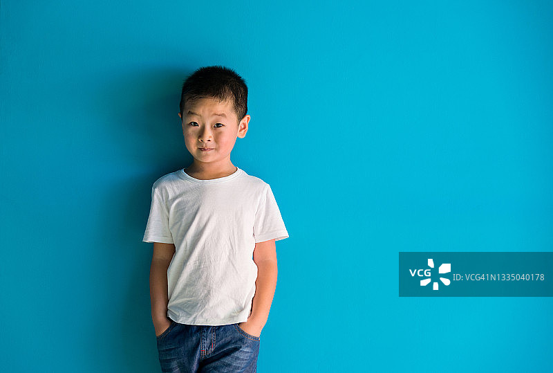 一个可爱的男孩站在蓝色的墙前图片素材