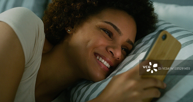 一名年轻女子晚上躺在床上使用手机图片素材