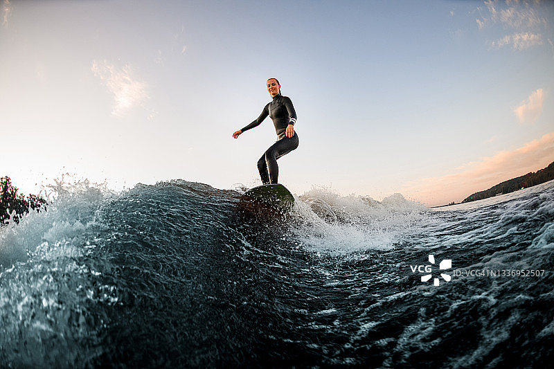 运动女子在冲浪板上沿河冲浪，背景是蓝天图片素材