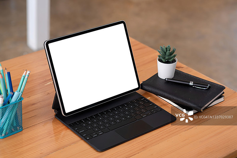 平板电脑空白的白色屏幕与工作设备放置在木制的办公桌。模拟。图片素材