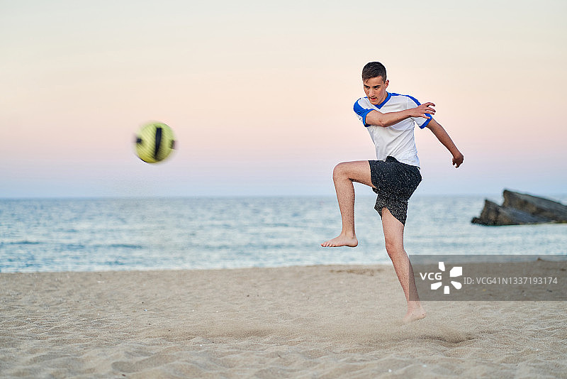 一个十几岁的男孩在沙滩上踢球图片素材