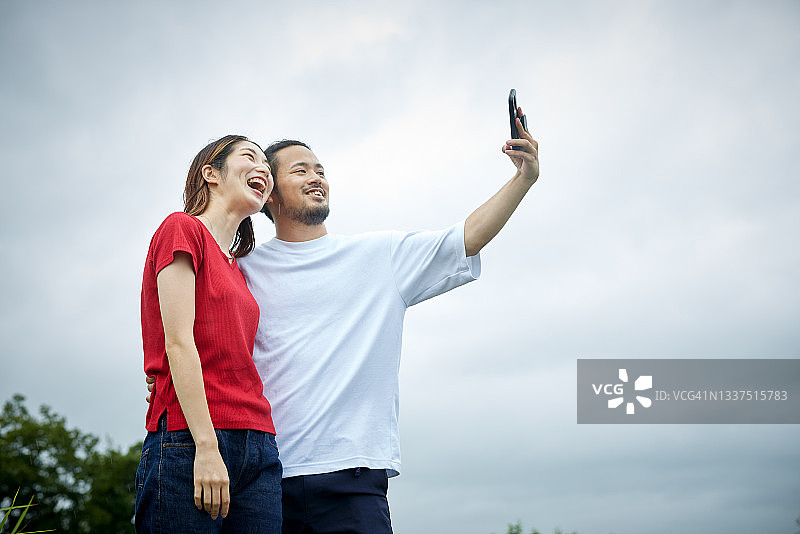 这是一对年轻夫妇在草地上用移动设备拍摄的照片。图片素材