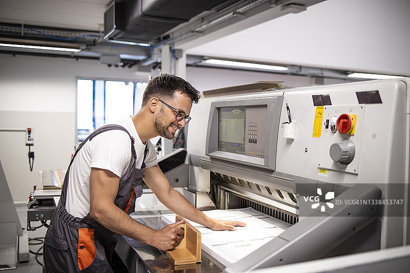 印刷厂的工人们在切割机上把一堆纸排好。图片素材
