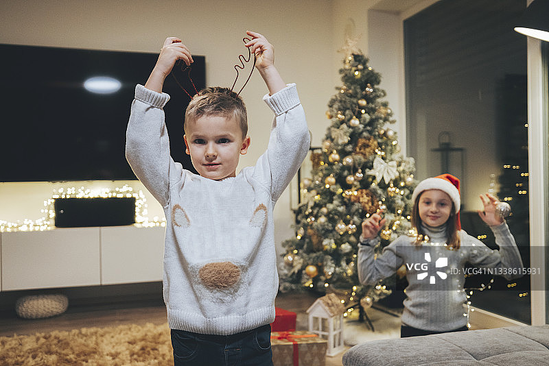 小男孩戴着驯鹿头带，背景是他的妹妹戴着圣诞老人的帽子图片素材
