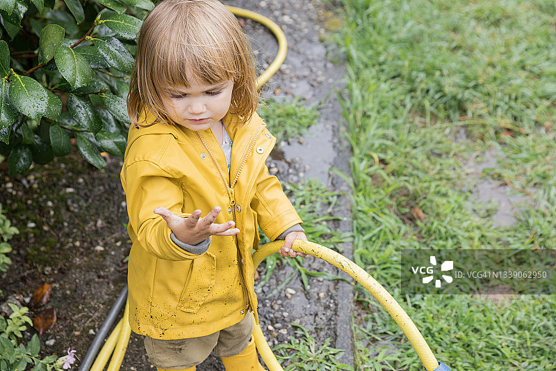 小女孩穿着雨衣，用水管给花园浇水。图片素材