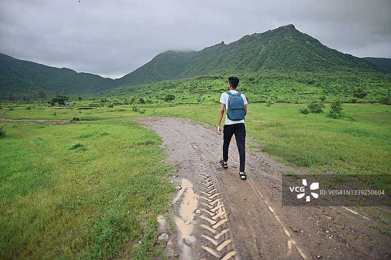 一个年轻人走在山峦环抱的泥泞小路上图片素材