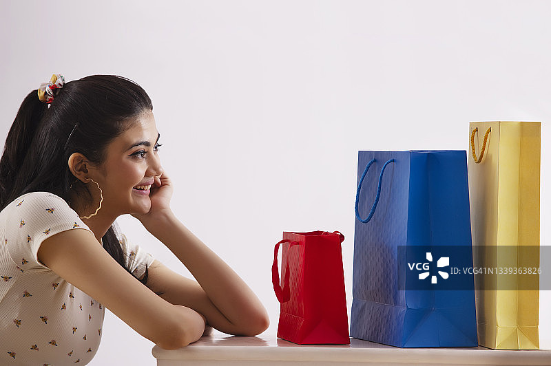 一个年轻的女人高兴地看着她五颜六色的购物袋。图片素材