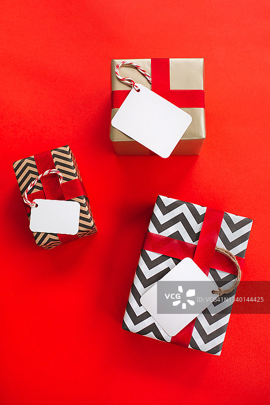 三个不同的礼品盒，白色标签，红色背景上有复制空间。新年庆祝概念。俯视图图片素材