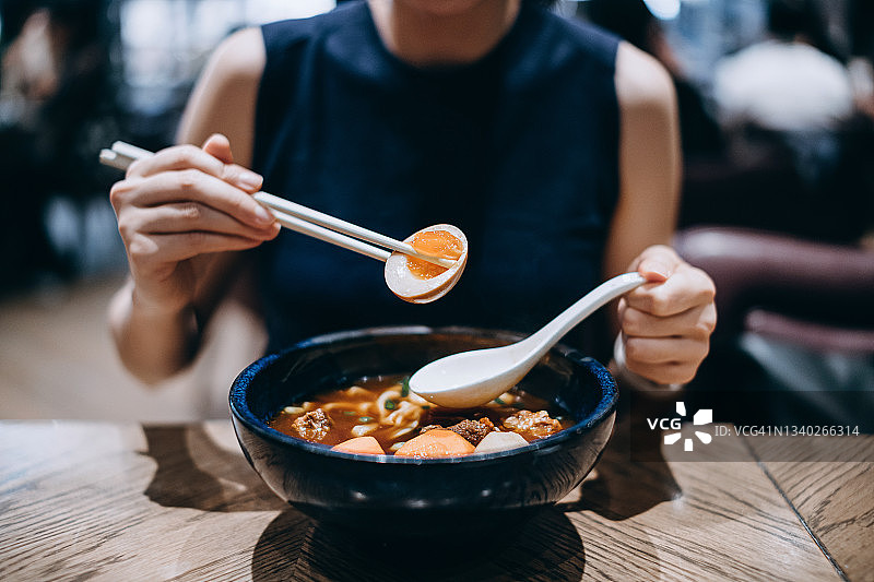 镜头靠近，一名年轻的亚洲女子正在餐厅享用一碗台湾风格的牛肉面。亚洲美食和饮食文化。外出就餐的生活方式图片素材