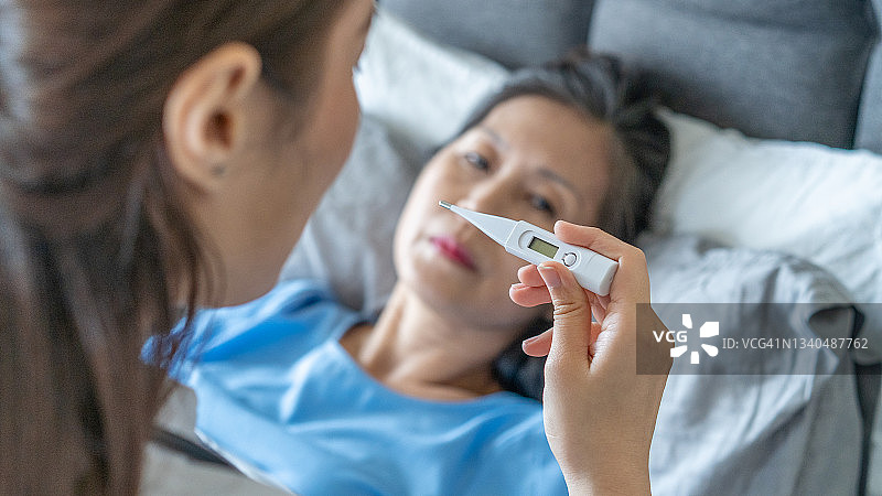 年轻的亚洲女医生拿着体温计在家中为成年女性量体温图片素材