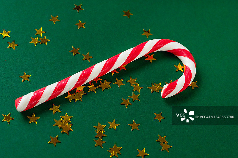 圣诞条纹红白相间的糖果，撒成金色星星的五彩纸屑，在美丽的绿色节日背景上。快乐圣诞节的概念。图片素材