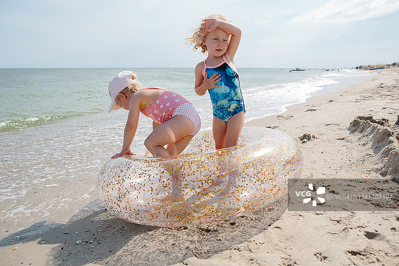 两个金发的初学走路的姐妹在海滩上的游泳圈上玩耍图片素材