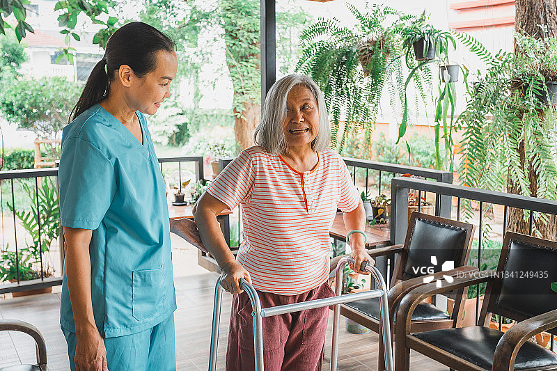 亚洲家庭保健工作者帮助老年妇女使用助行器行走图片素材