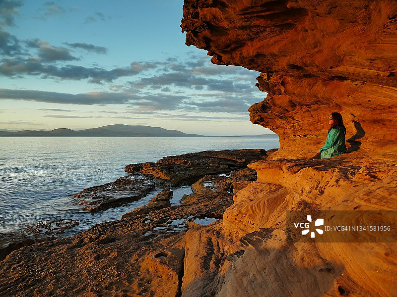 澳大利亚塔斯马尼亚，莱姆湾，日落时分，坐在红色砂岩悬崖边的女人图片素材