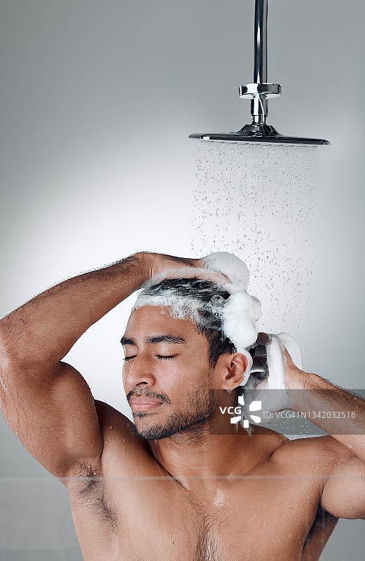 一个年轻人在淋浴时洗头发，背景是灰色的图片素材
