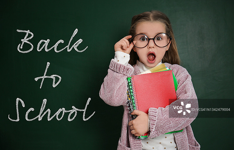 可爱的小男孩戴着眼镜，旁边是写着“回到学校”的黑板图片素材