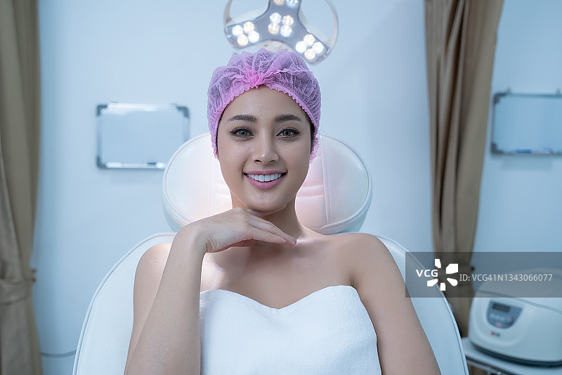 年轻女性客户的肖像在美容诊所白色头巾坐在床上检查她的美丽的脸。图片素材