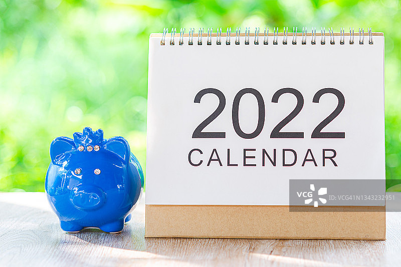 蓝色小猪储蓄罐和日历桌2022节省钱或工资支付日的计划和提醒在木制桌子上的自然背景。图片素材