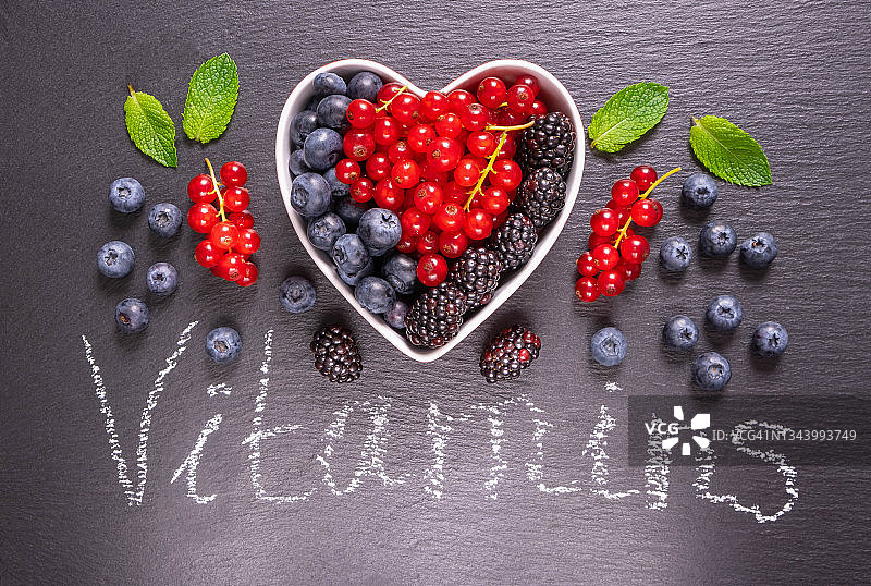 满碗，心形，成熟的蓝莓，醋栗，黑莓，薄荷叶和浆果散落在黑色背景上的铭文图片素材