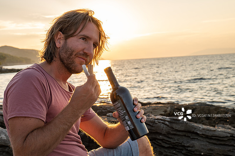 日落时分，一个年轻人在海边喝红酒图片素材