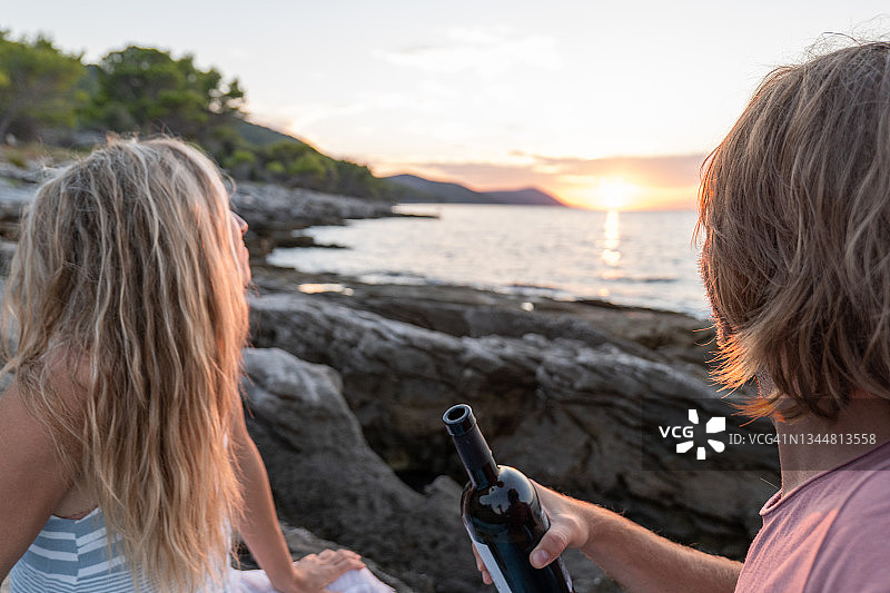 年轻夫妇在日落时在海边喝酒图片素材