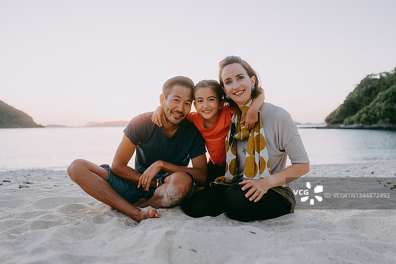 日本，日落沙滩上，一家人带着一个孩子对着镜头微笑图片素材