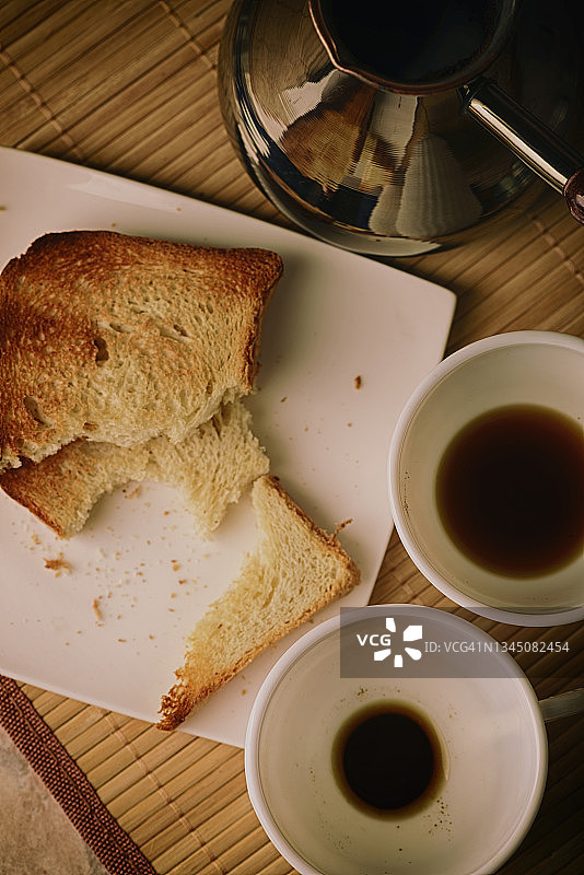 咖啡被倒进白色的杯子里。烤面包。早餐在桌子上。图片素材