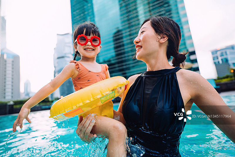 快乐的亚洲小女孩戴着太阳镜快乐地微笑着，享受着与母亲的家庭亲密时间，在暑假的游泳池里玩得很开心图片素材