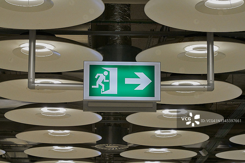 马德里机场的屋顶悬挂着许多灯，还有一个绿色的“逃生路”标志。马德里机场的屋顶上悬挂着一些灯，一个逃生通道的标志打开了。图片素材