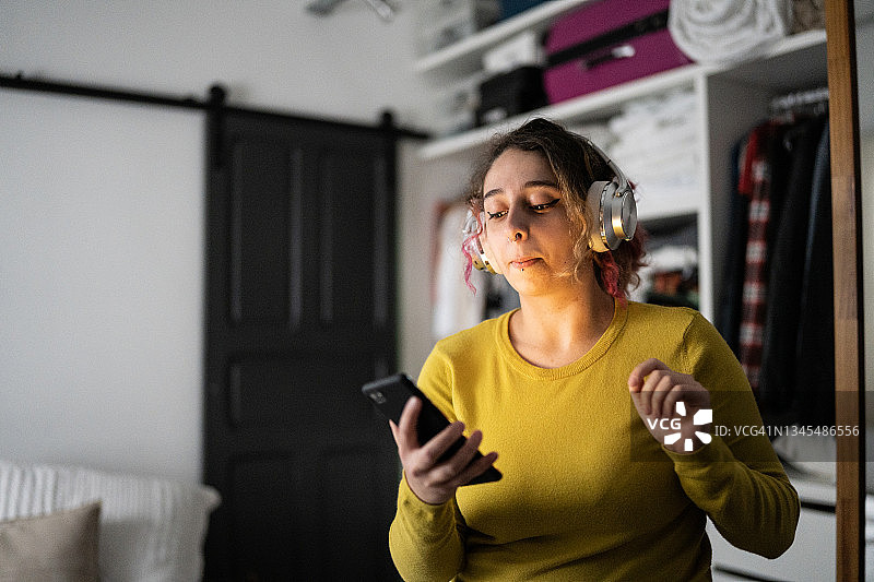 年轻女子戴着耳机在手机上听音乐，在家跳舞图片素材