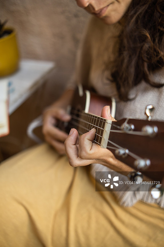 一个女人的手在她的房子的阳台上演奏着木制的弦乐器，这是一个放松的时刻。图片素材