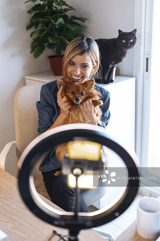 微笑的女视频博主与狗影响在家里图片素材