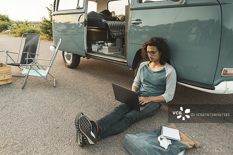 一个人坐在露营车旁边用笔记本电脑图片素材