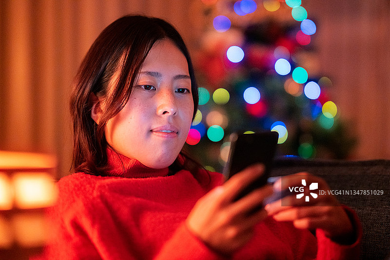 一名年轻女子在圣诞节晚上在家用智能手机网购图片素材
