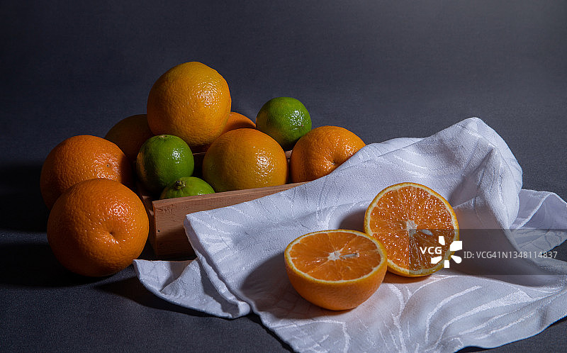 柑橘静物画，在灰色背景的白色餐巾上切成两半的橙子。图片素材