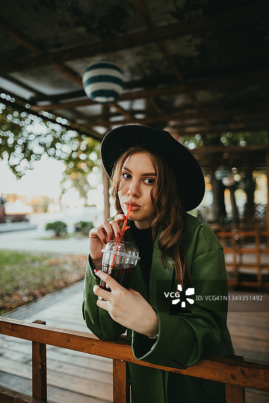 一个时尚的女人戴着帽子在户外喝果汁图片素材